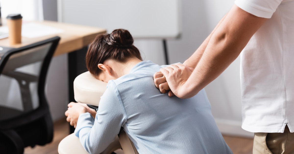 Closeup of a woman sitting in a massage chair in an office environment getting a back massage from a massage therapist.